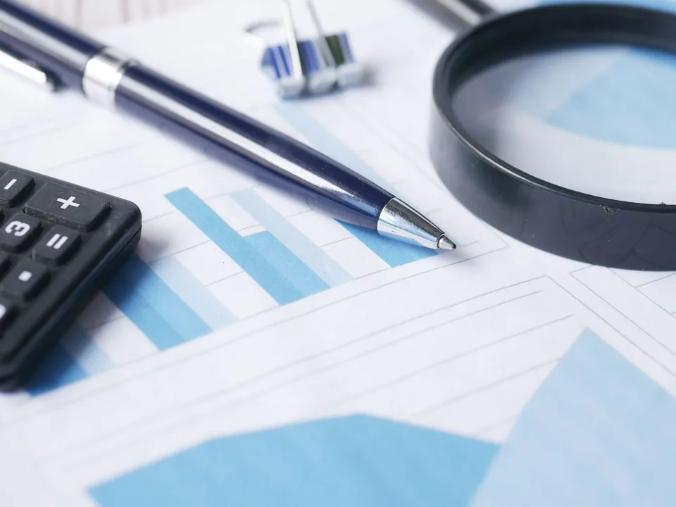 Lupa, calculadora y bolígrafo sobre un gráfico financiero, representando la auditoría externa del SPARLAFTD