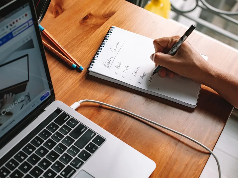 Persona tomando notas junto a un computador portátil mientras revisa cursos de formación en línea