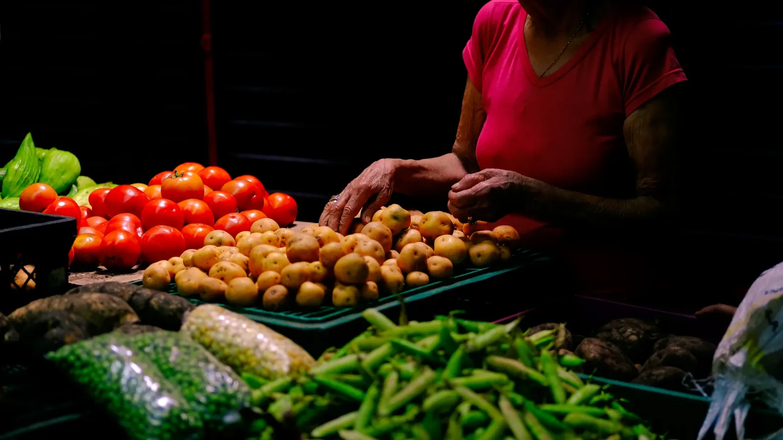 Manos de una comerciante ordenan papas junto a tomates y arvejas en un puesto de mercado en Colombia