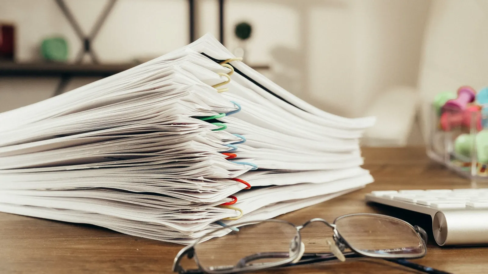Pila de documentos comerciales sujetos con clips de colores sobre un escritorio de oficina