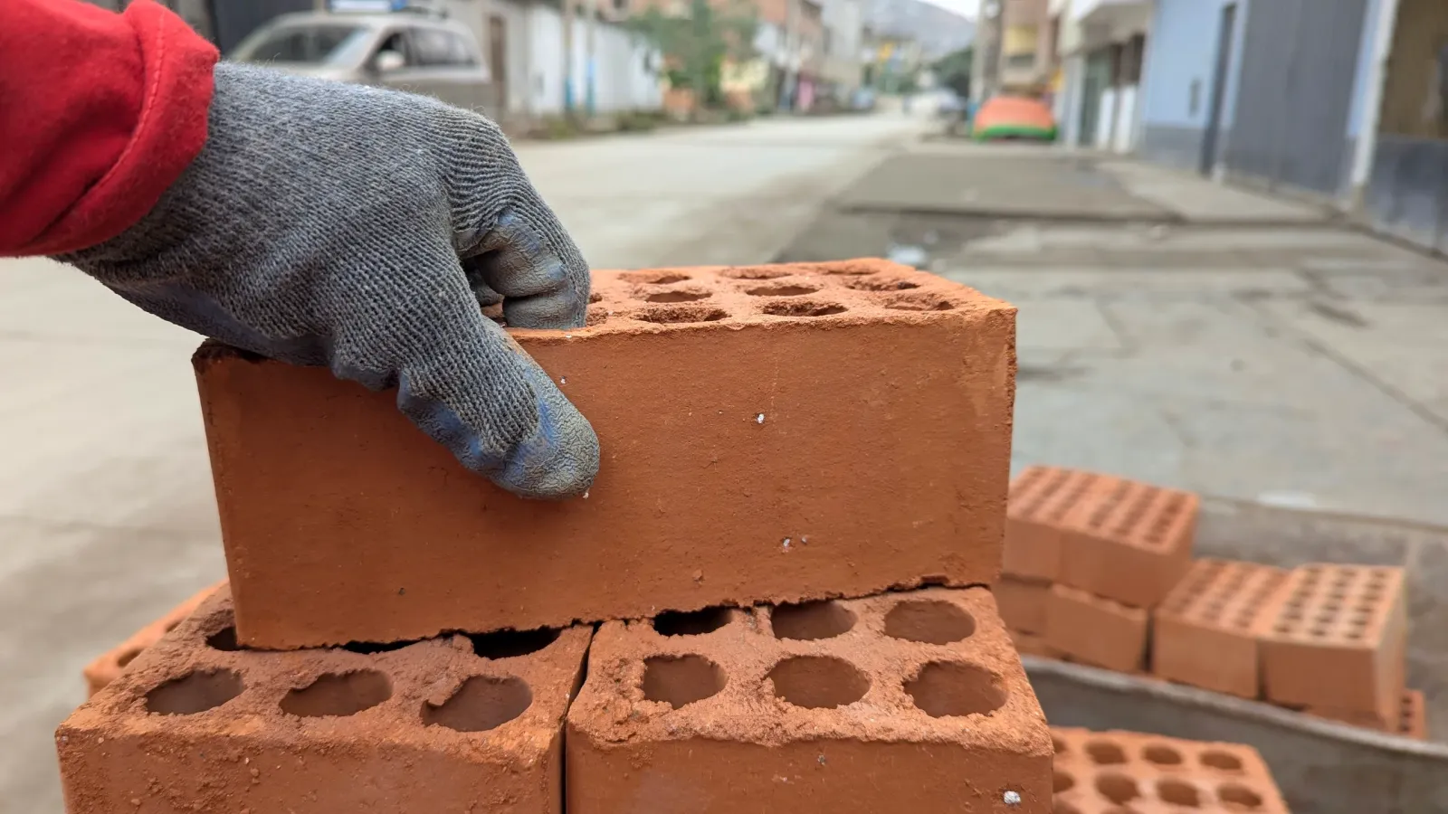 Mano con guante coloca un ladrillo de arcilla sobre una pila en una calle en obras