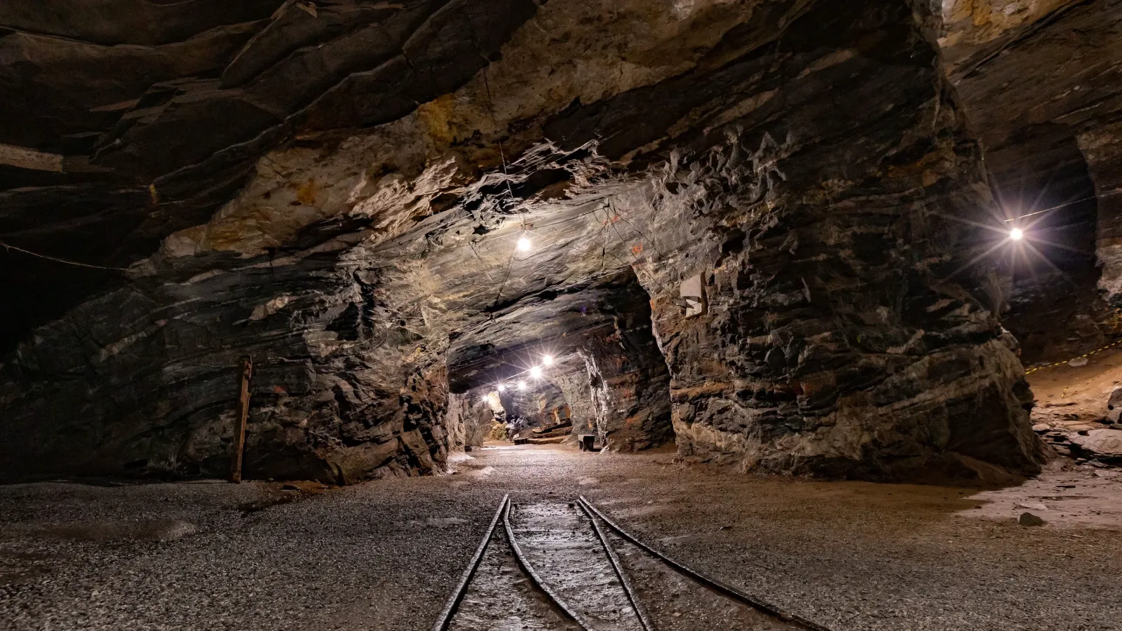 Galería subterránea de una mina con rieles en el suelo e iluminada por lámparas