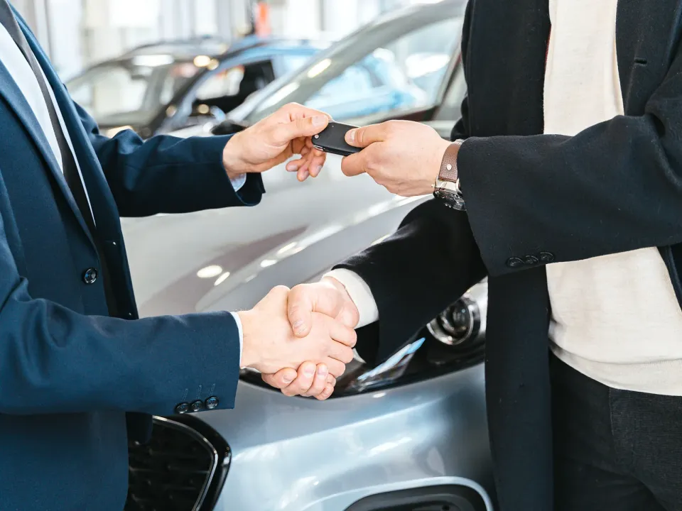 Entrega de la llave de un auto nuevo con apretón de manos en la sala de un concesionario