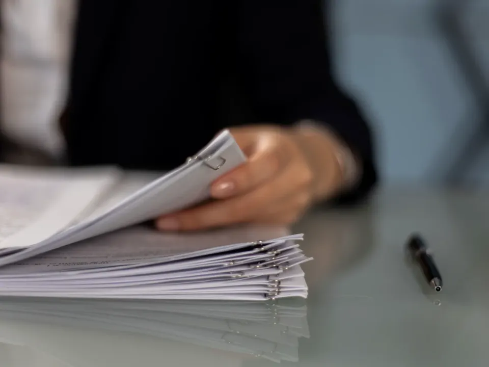 Mano revisando un legajo de documentos sujetos con clips sobre un escritorio de vidrio