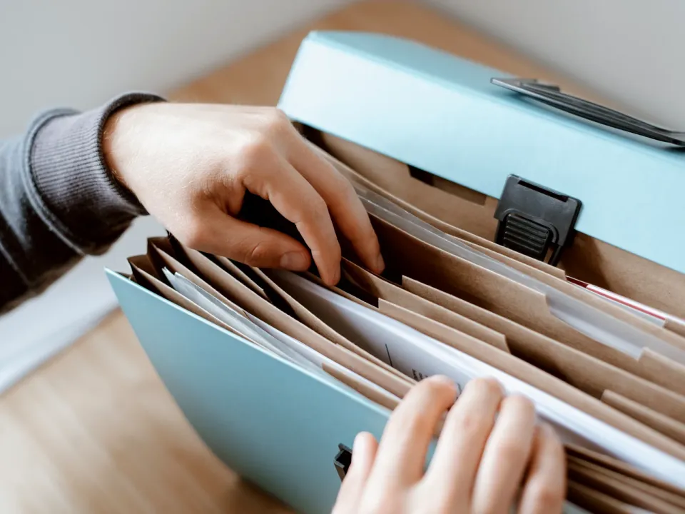 Hands looking for a file inside an accordion folder full of documents