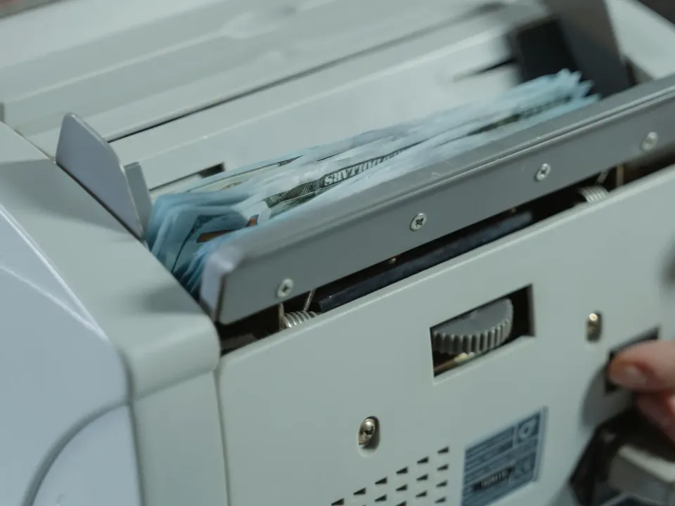 Máquina contadora procesando un fajo de billetes, con la mano del operador en el lateral