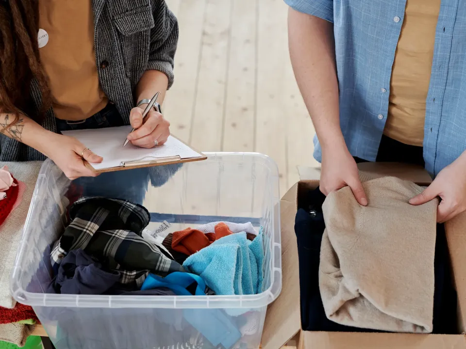 Two volunteers log donated clothes on a clipboard as they sort them into boxes