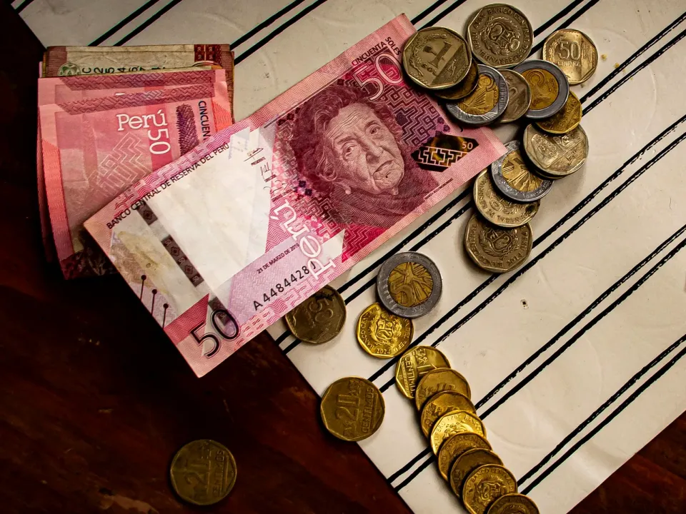 Billetes de 50 soles y monedas peruanas apiladas sobre un mantel a rayas
