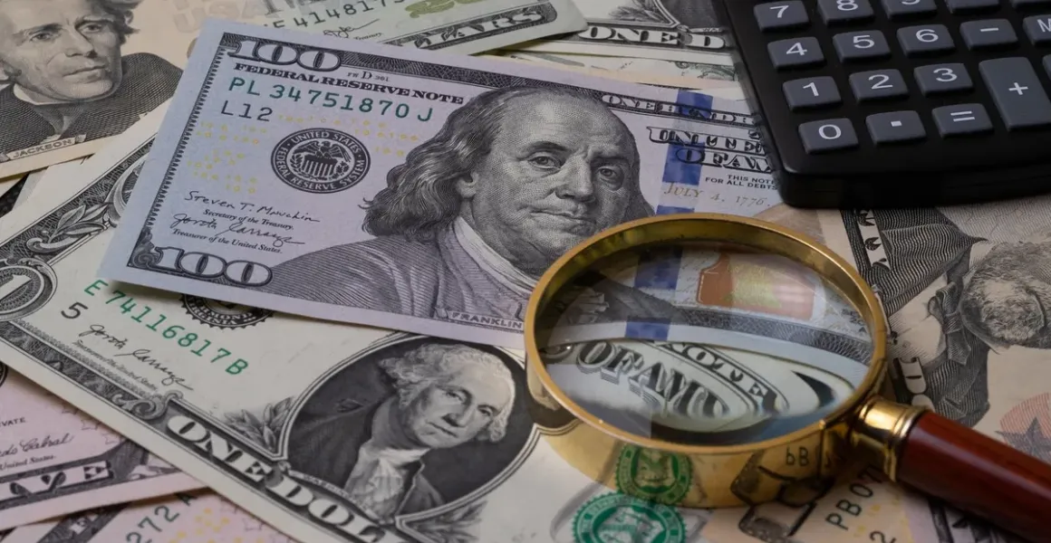Dollar bills examined with a magnifying glass and calculator, representing financial analysis of illegal fundraising as a predicate offense to money laundering