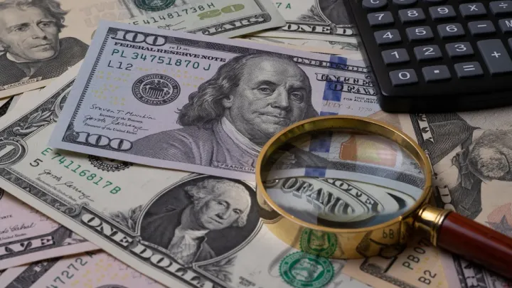Dollar bills examined with a magnifying glass and calculator, representing financial analysis of illegal fundraising as a predicate offense to money laundering